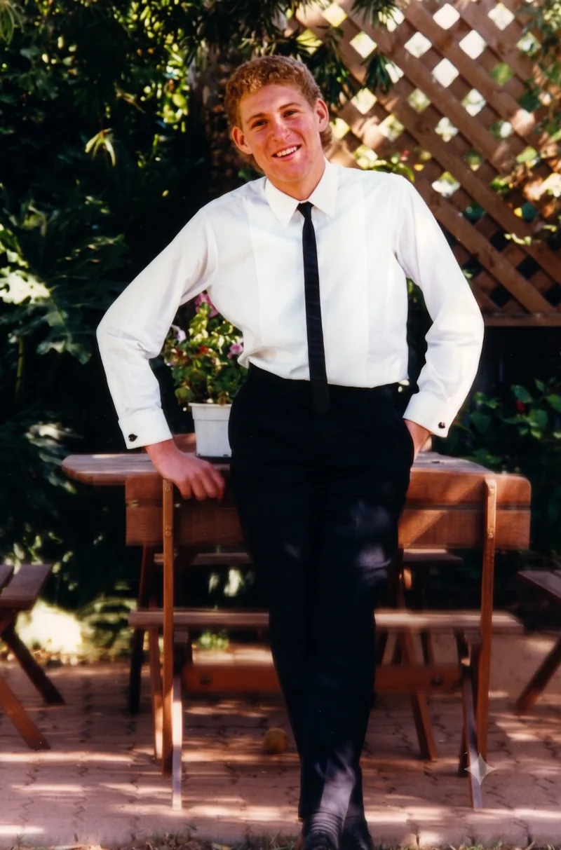 Teenage boy in white shirt and black tie standing in a backyard, smiling, Pooraka, Adelaide, 1988. Digitally restored version.