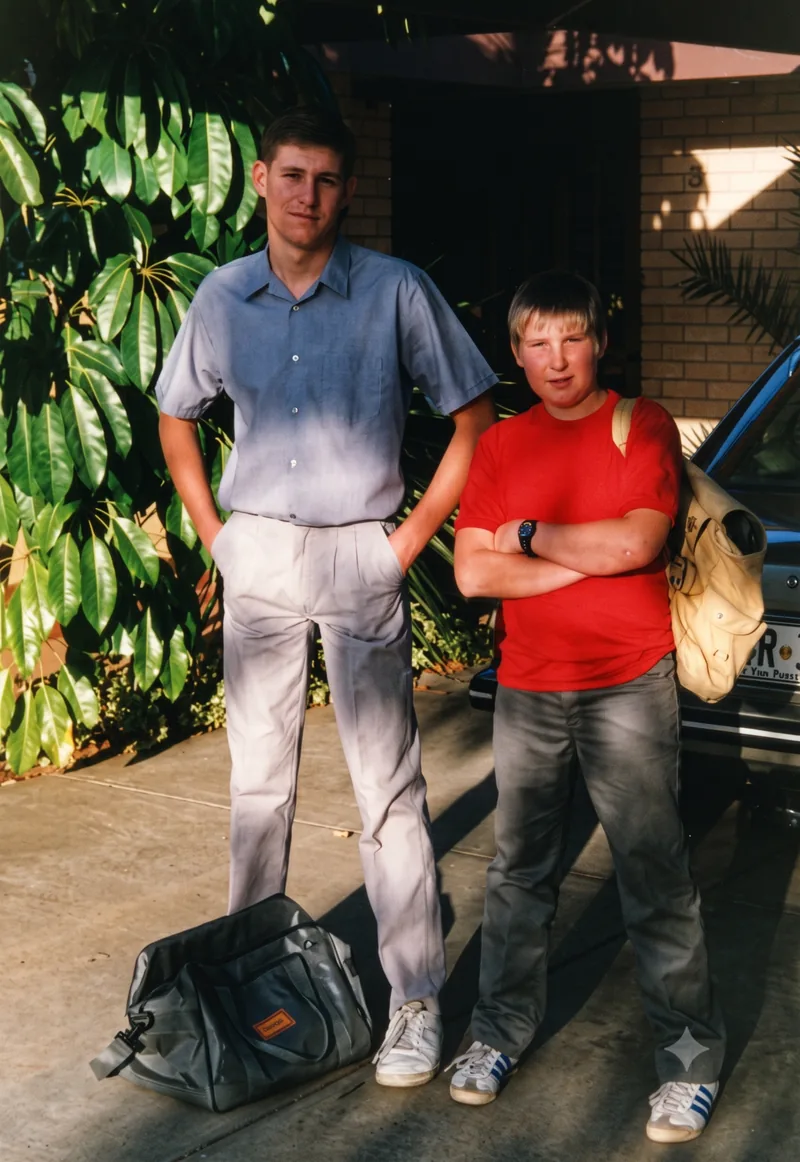 Two teenage boys with school bags standing in front of a brick house, Pooraka, Adelaide, early 1989. Digitally restored version.