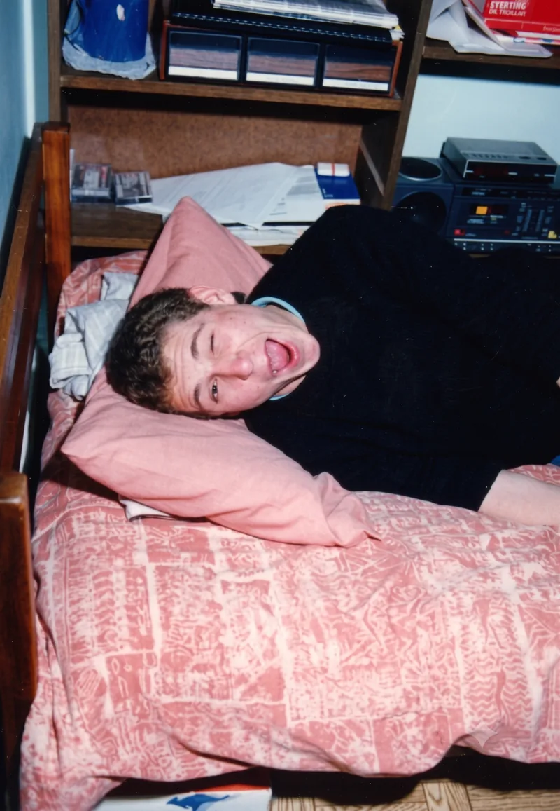 Teenage boy lying on a bed with tongue out, looking unwell, bedroom with stereo and shelves, Pooraka, Adelaide, c. March 1991. Digitally restored version.